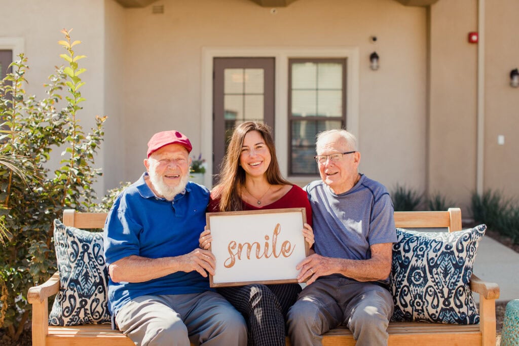 woman sitting between two men holding sign that says smile